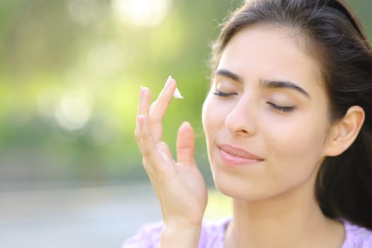 Beautiful woman hydrating face skin with cream in a park