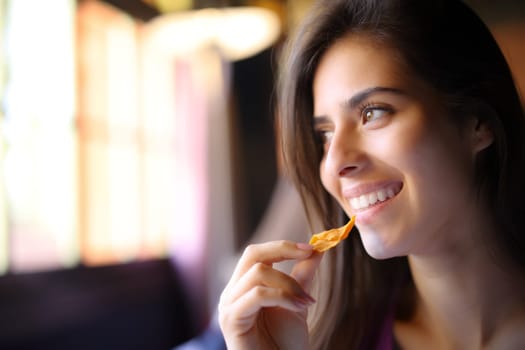 Happy restaurant customer eating chips looks at side through a window