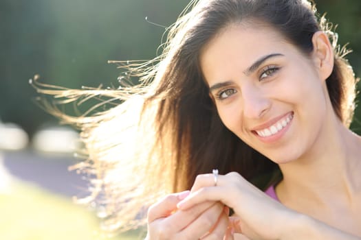 Happy fiancee showing engagement ring looking at camera in a park