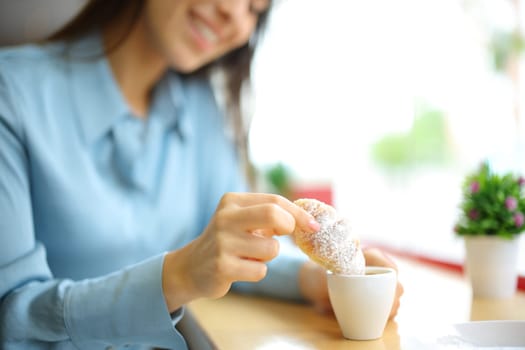 Happy woman dipping croissant in a coffee cup in a restaurant