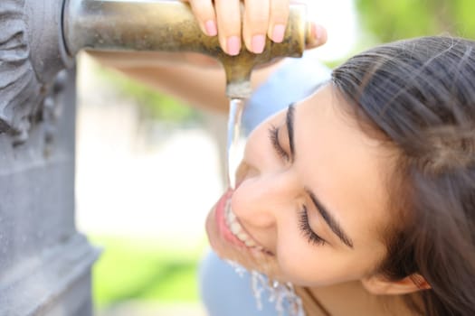 Happy woman drinking water from public fountain in the street
