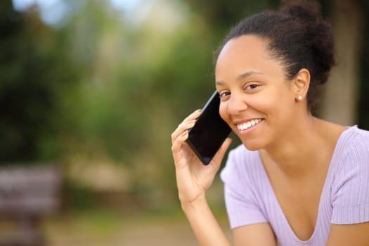 Happy black woman calling on phone looking at you in a park