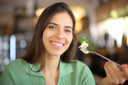 Happy woman holding fork with lettuce in a restaurant looking at camera