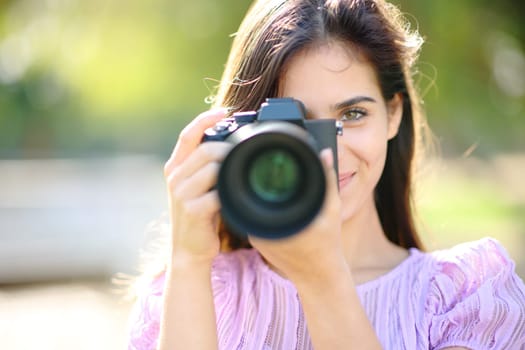Front view portrait of a happy photographer taking picture of you in a park