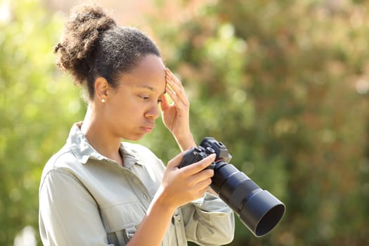 Worried black photographer checking camera content in a park