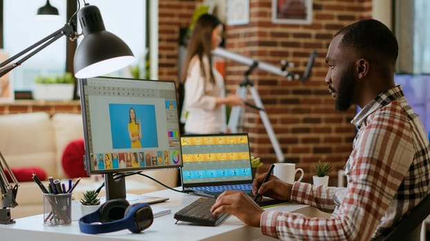 African american photo editor retouches images on his computer in a tech inspired workspace. Man does freelance tasks for photo retouching and digital art, media and graphic design sectors. Camera B.
