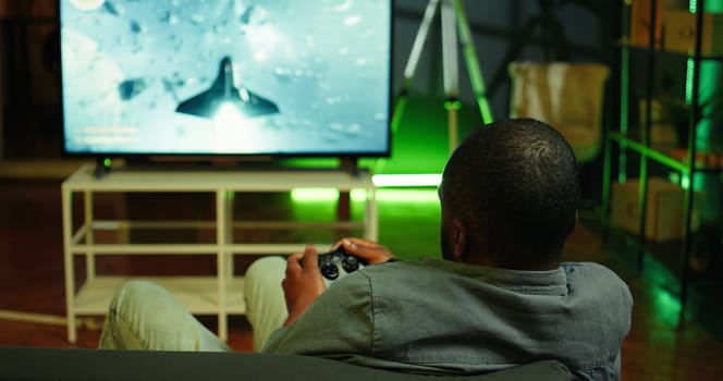 Man playing SF videogames on gigantic smart TV, relaxing after long day at work. Competitive gamer having fun on gaming console in apartment, piloting spaceship using controller, camera B