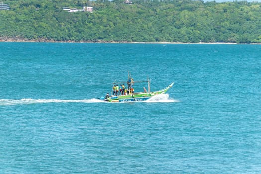 Galle Sri Lanka - September 14 2024; Local fishing boat or oruwa named Silent Heat loaded with men in bright clothes motors across bay.