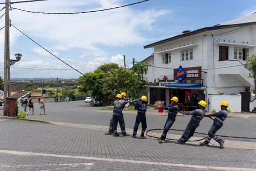Galle Sri Lanka - September 14 2024; Workers from Ceylon Electric Power standing in row with yellow hard-hats pulling a power-line into place.