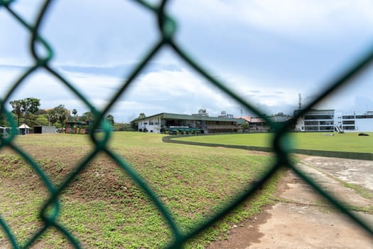 Galle Sri Lanka - September 14 2024; View through chain link fence around Galle Cricket field with Cricket Club stand in readiness for test game.