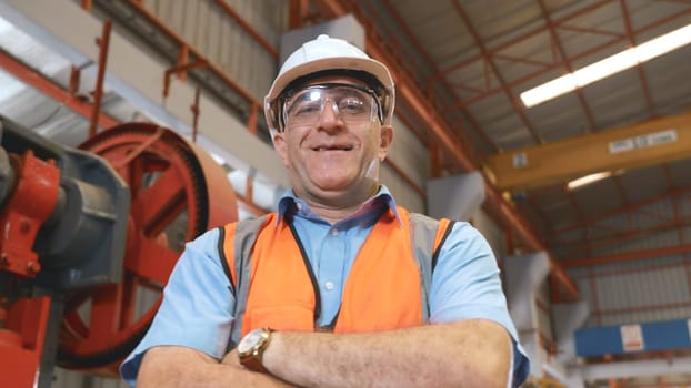Portrait of senior man worker in safety uniform of large modern factory crossing arms on chest, Smiling and happy employee at Metal sheet stamping machine while working at industrial production plant