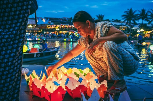 An elderly Vietnamese woman sells paper lanterns for festive festival by the river in old town in Hoi An city in Asia. Hoi An, Vietnam - December 1, 2024