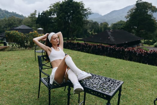 A young fitness model with sporty attire poses outdoors, embodying a healthy lifestyle in a summer environment, with lush greenery and mountains in the background