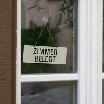 Sign on the entrance door of a hotel with the German inscription Zimmer belegt. Translation: Rooms occupied