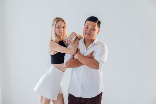 Asian man and blonde woman smiling and hugging together on white background