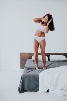 Brunette in lingerie listening to music in headphones and dancing in bedroom on bed