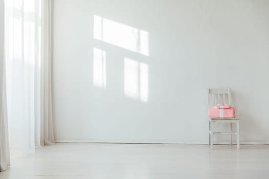 Old chair with pink gift in the interior of a white room with a window
