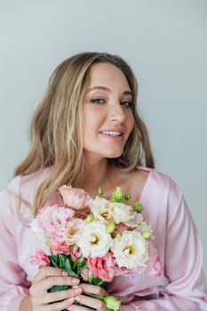 Fashionable woman in summer pink dress with bouquet of spring flowers in white room