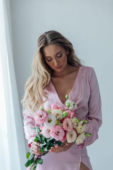 Fashionable woman in summer pink dress with bouquet of spring flowers in white room
