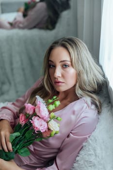 Fashionable woman in summer pink dress with bouquet of spring flowers in white room