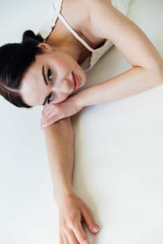 Brunette woman in white dress lying on bed and smiling