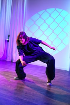 A dancer showcases their unique style in a contemporary dance studio, featuring vibrant purple lighting and textured backgrounds. The atmosphere is dynamic and energetic.