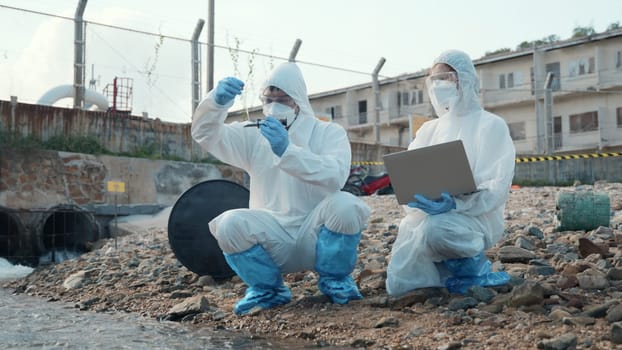 Ecologist sampling water from the river to water quality tester and peek into, Biologist wear protective suit and mask collects sample of waste water from industrial for pH meter, problem environment