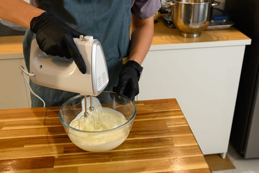 Gloved hands using electric hand mixer to whip cream in glass bowl for compound butter.