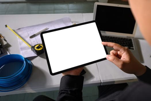 Engineer holding digital tablet with blank white screen at construction planning table.