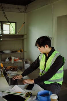 Engineer using laptop to review plans and manage site progress in a home renovation.