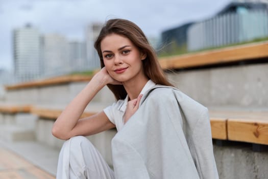 Casual young woman in light clothes poses smiling outdoors against modern urban background, showcasing relaxed confidence, natural beauty, soft light, and autumn atmosphere