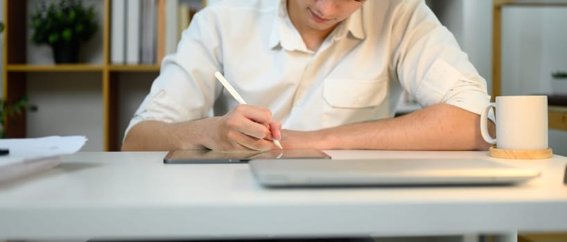 Close up of man using a stylus to taking notes on digital tablet at modern office desk.