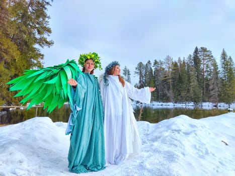 Two girls wear elegant dresses symbolizing winter and spring, standing in snow by a serene lake as they represent the transition of seasons.