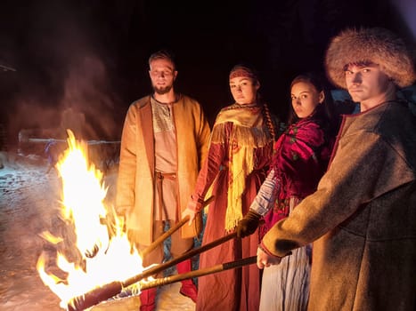 Actors in ethnic costumes demonstrate a captivating fire show on a frosty winter night, embodying Viking warrior spirits in their performance.