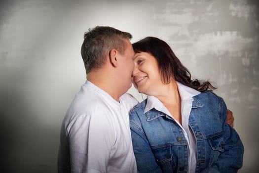 A middle-aged couple shares a joyful moment, smiling and embracing in their cozy apartment during a casual photo shoot indoors.