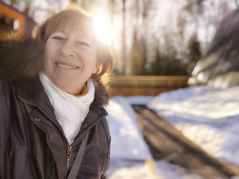 A middle aged female blogger smiles for a selfie while exploring a beautiful snowy landscape on a sunny winter day.