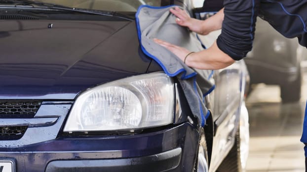 Car wash worker drying a clean vehicle with a microfiber cloth, car detailing and cleaning service