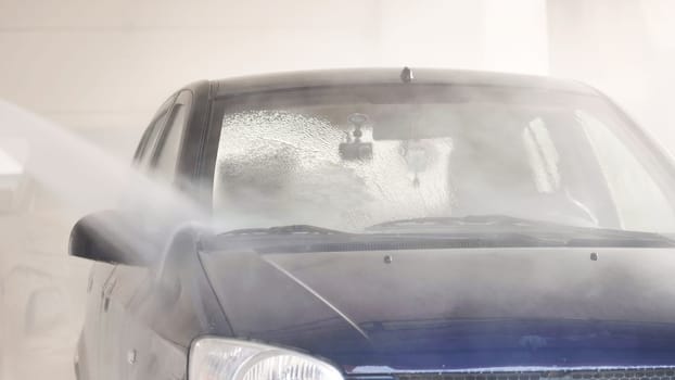 Automatic car wash is cleaning windshield of car with powerful water jet