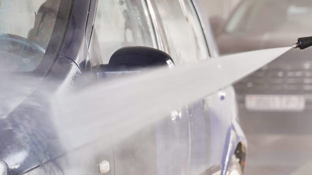 Car wash worker cleaning vehicle with high pressure water jet