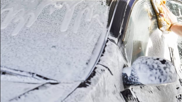 Car wash worker is cleaning a vehicle with a sponge and soap
