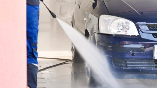 Car wash worker cleaning front bumper of automobile with high pressure water jet