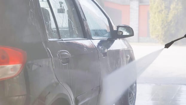 Worker washing a car with high pressure water jet in a car wash