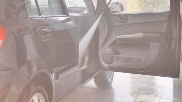 Car wash worker is cleaning vehicle interior with high pressure water jet