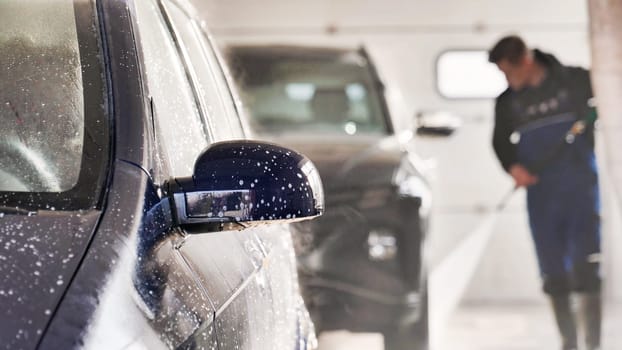 Professional car wash worker cleaning vehicle with high pressure water jet in a car wash service station