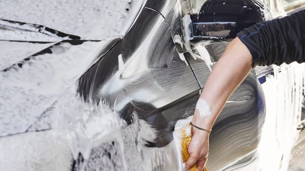 Car wash worker is cleaning a vehicle with a sponge and soap foam