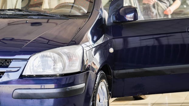 Car wash worker is cleaning a vehicle with a high pressure water jet