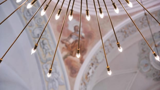 Modern chandelier illuminating ancient church ceiling with religious frescoes