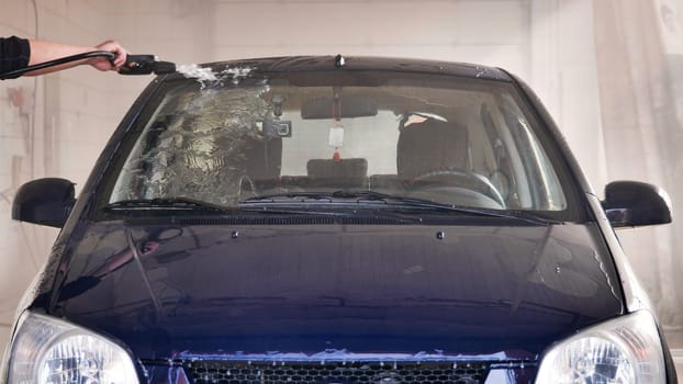 Car wash worker spraying water on a car windshield with a high pressure washer