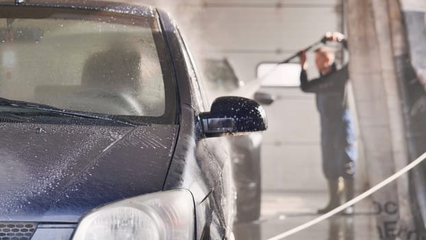 Car wash employee spraying foam and water on automobile during cleaning service
