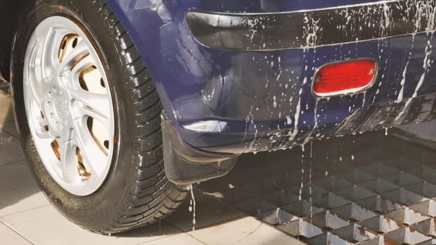 Soap dripping from the bumper of a blue car being washed